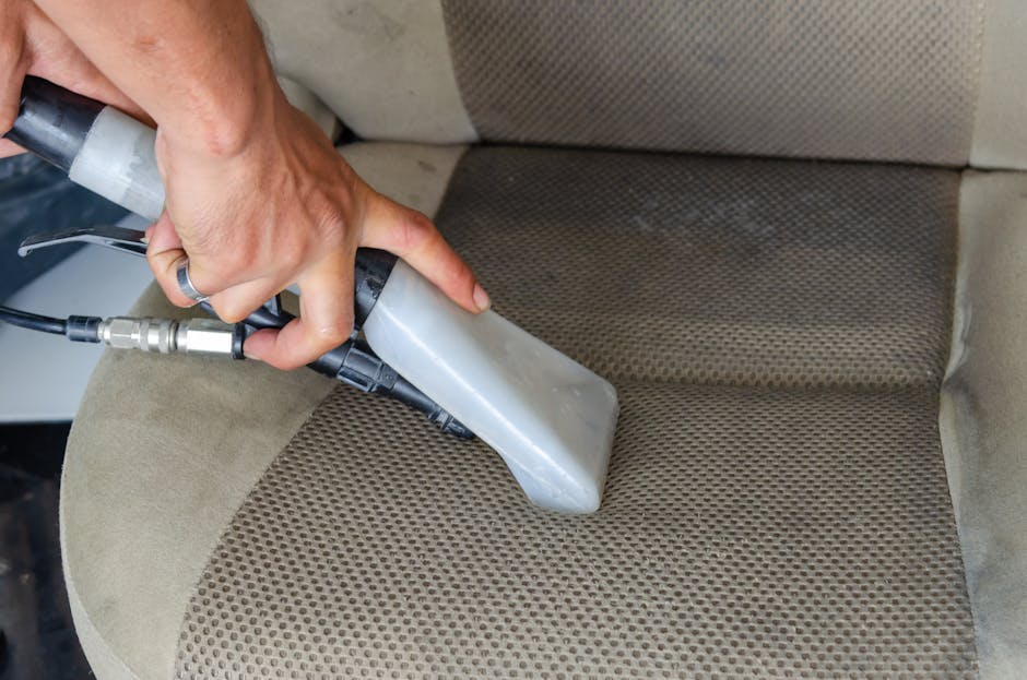 A person vacuuming a large, ornate area rug with a yellow canister vacuum cleaner in a well-lit room. The individual is wearing light-colored sneakers and casual clothing, holding the vacuum's wand at
